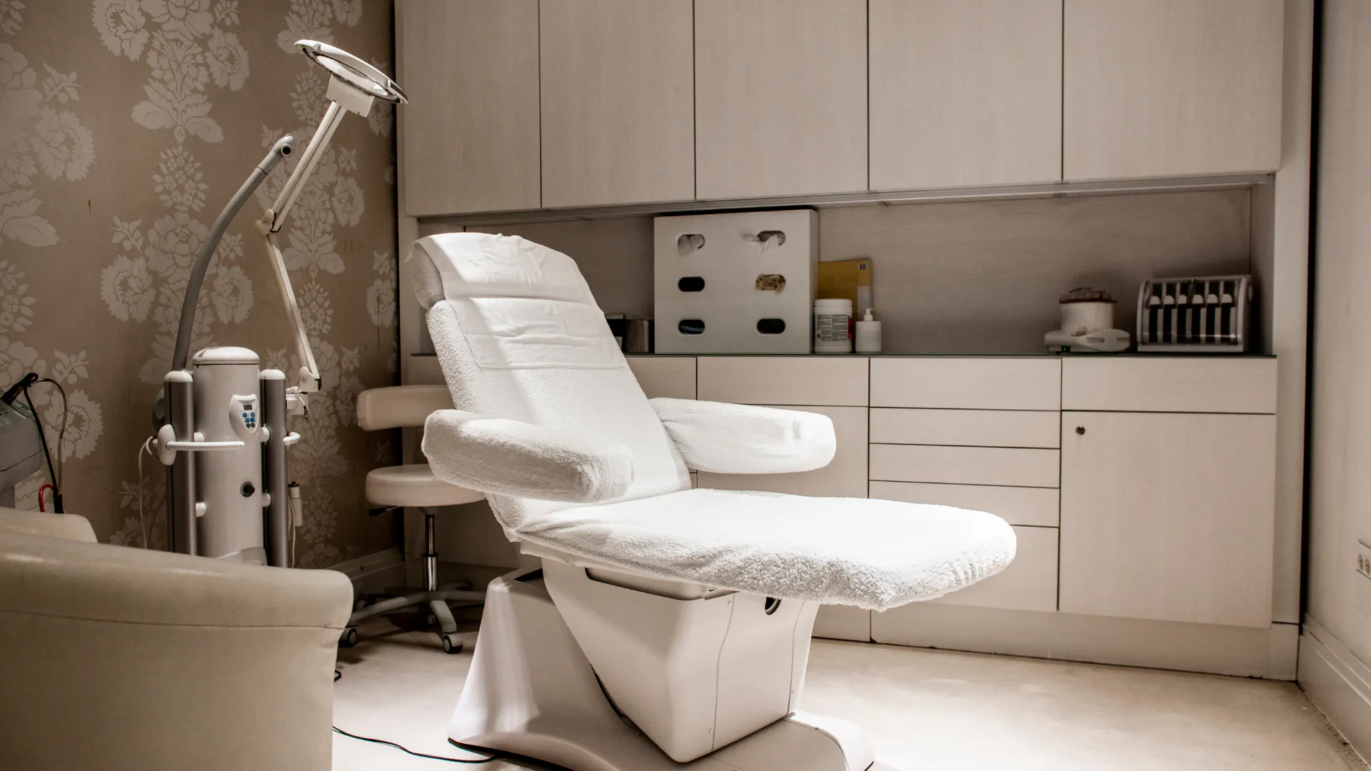 A private dermatology clinic treatment room with an examination chair and lamp